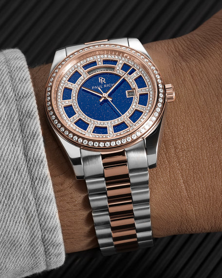 Two-tone silver and rose-gold watch with a blue aventurine dial, day and date windows, and a bezel and hour markers set with crystal stones.