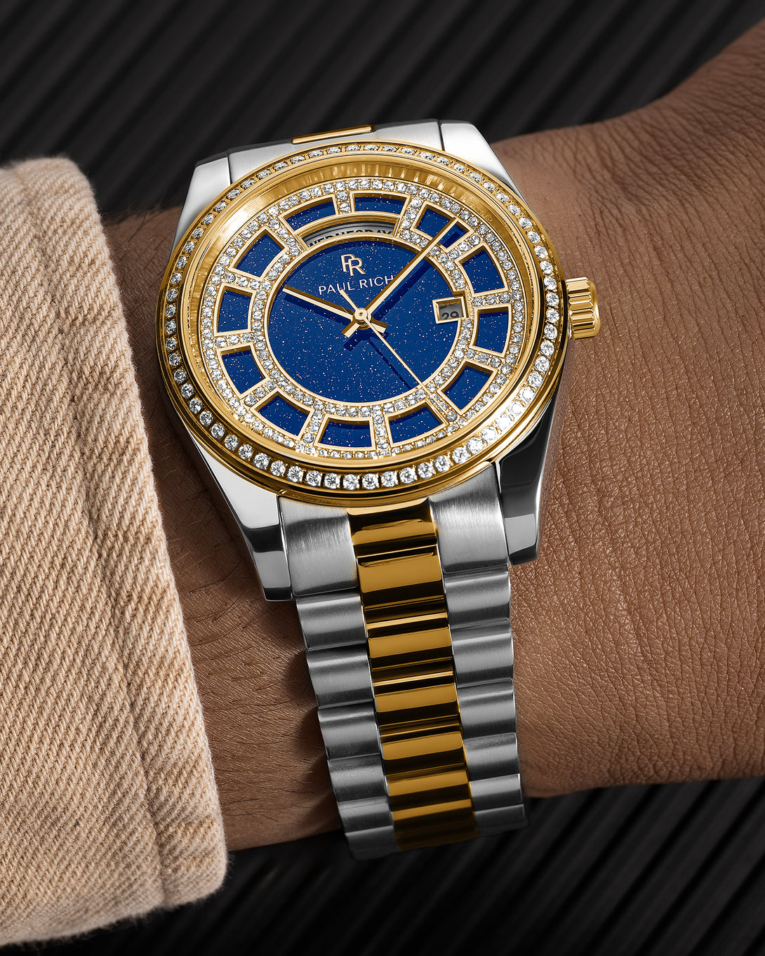 Two-tone silver and gold watch with a blue aventurine dial, pavé diamond bezel, and day–date display shown on a wrist with a matching bracelet.
