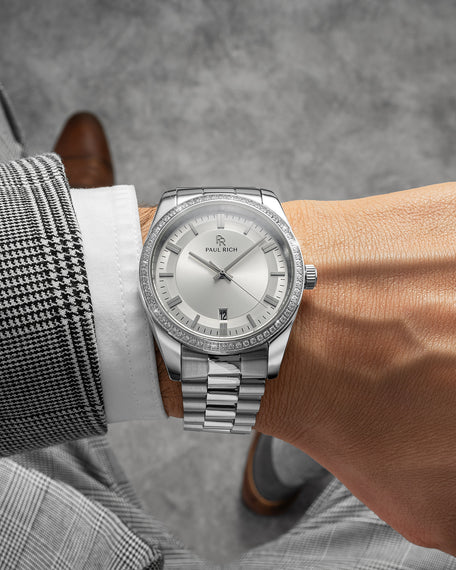 Silver watch with sunray dial, gem-set bezel, and jubilee bracelet, worn with a houndstooth suit and brown leather shoes.