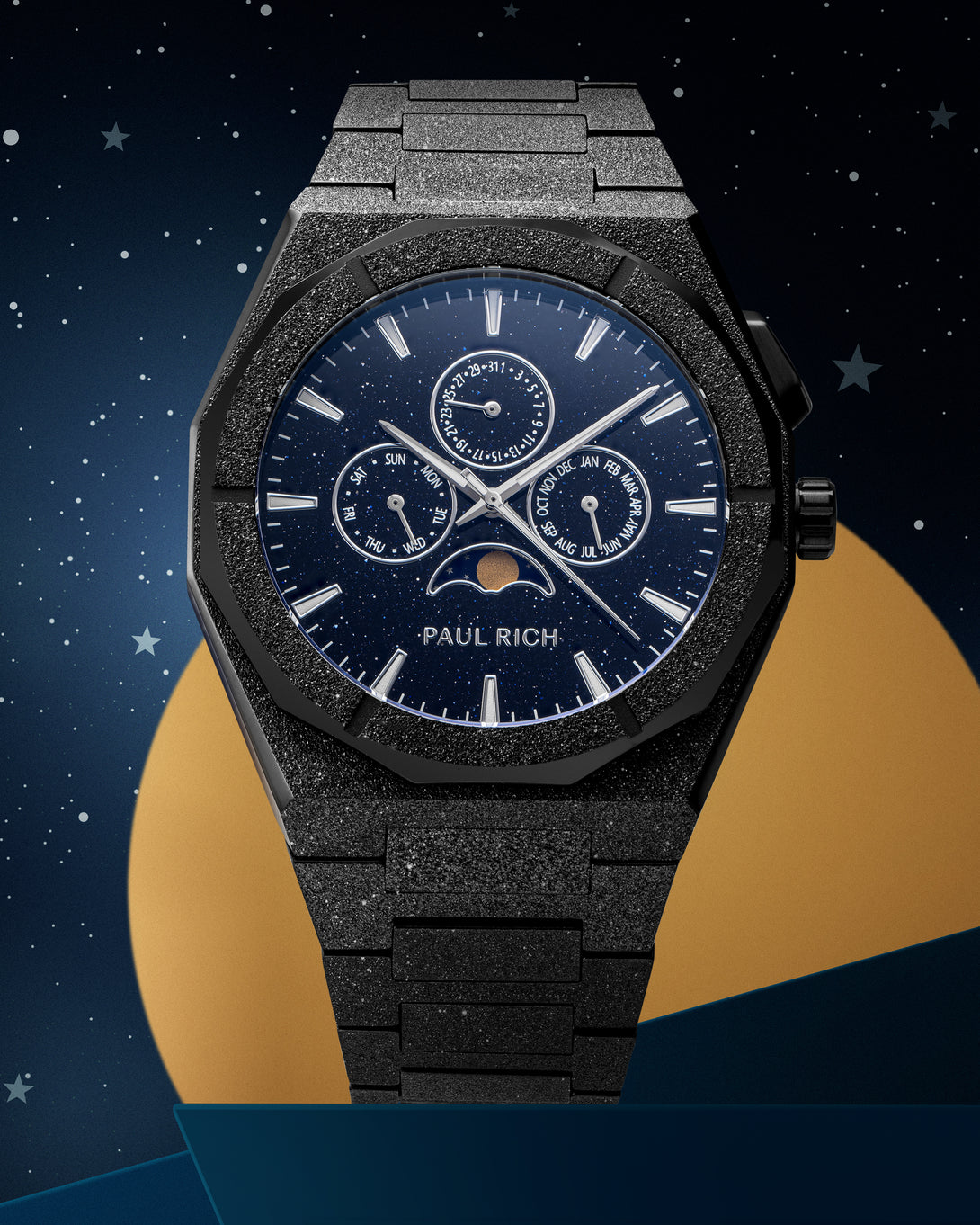 Frosted black stainless steel watch with blue aventurine dial, moonphase, and subdials, set against a starry night sky and gold circle backdrop.
