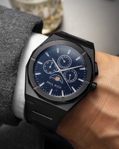 Brushed black moonphase watch on wrist with aventurine dial, calendar subdials, and black steel bracelet.