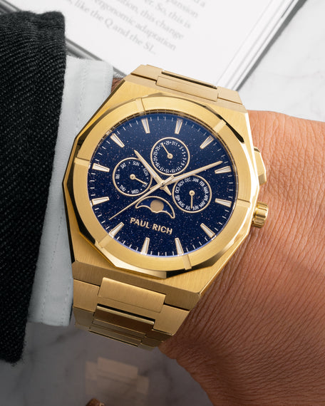 Brushed gold moonphase watch on wrist with deep blue aventurine dial, calendar subdials, and gold bracelet.