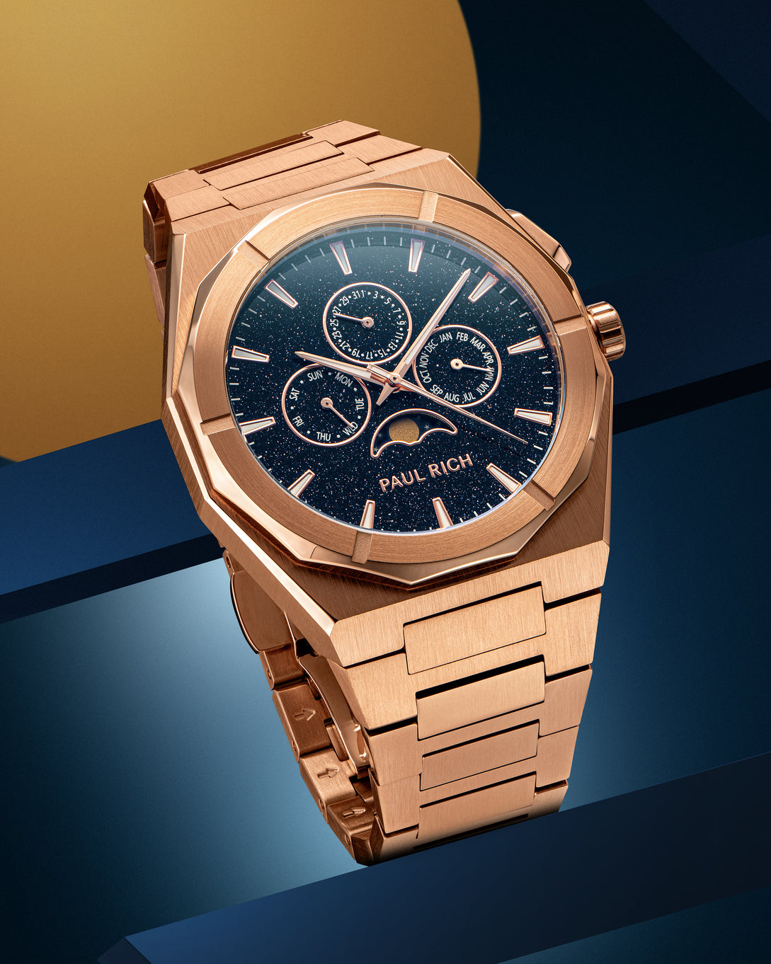 Rose gold-tone stainless steel watch with blue aventurine dial, moonphase, and subdials, displayed on a geometric blue and gold backdrop.