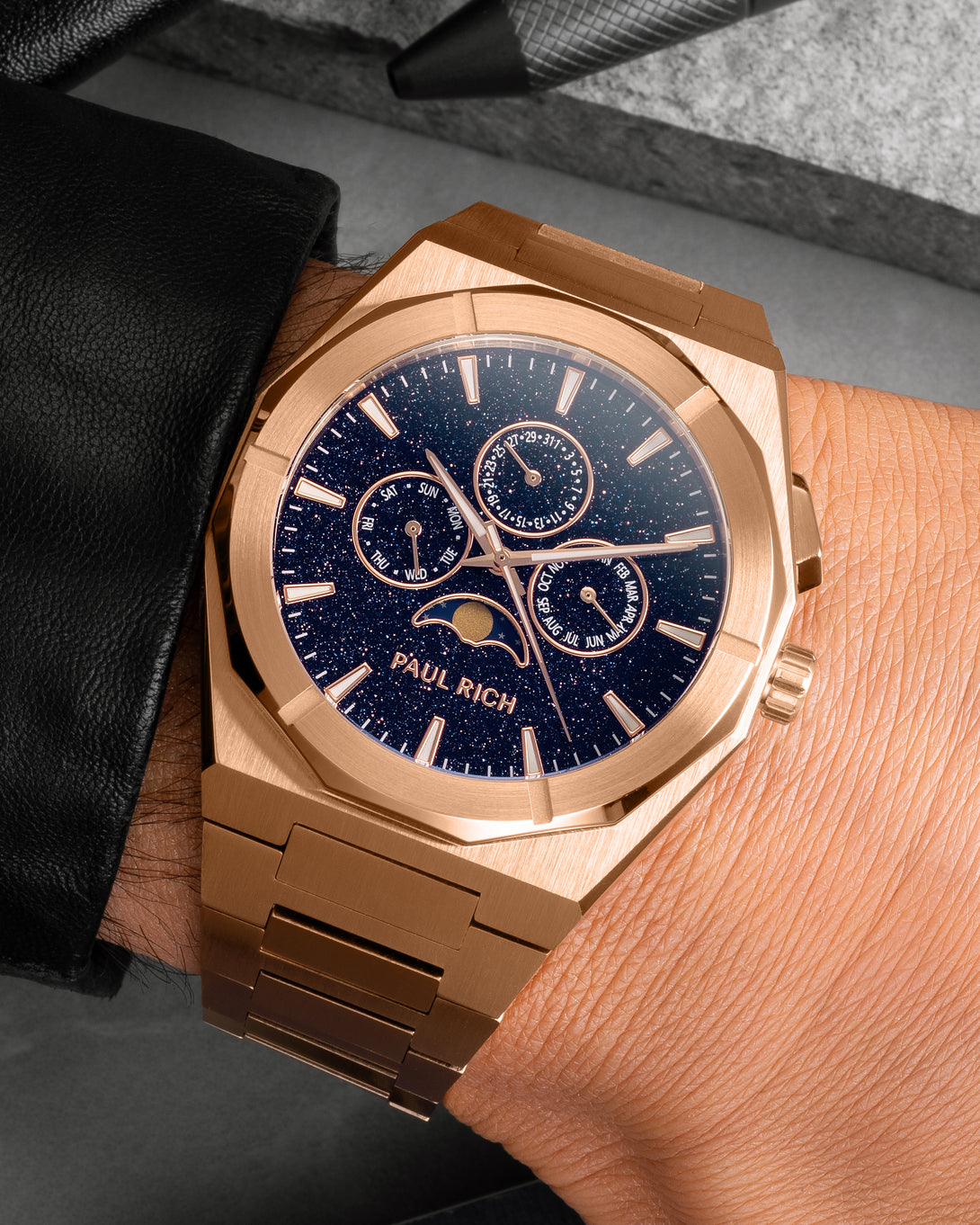 Rose gold moonphase watch on wrist with aventurine dial, day, date, and month subdials, brushed rose gold bracelet.