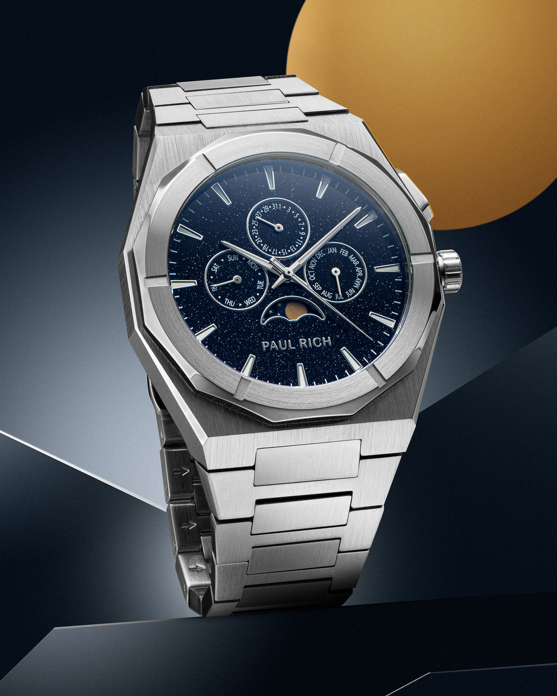 Silver stainless steel watch with blue aventurine dial, moonphase, and subdials, displayed on a geometric silver and blue backdrop with a gold circle.