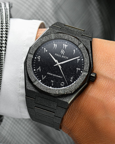 Close-up of Paul Rich frosted black watch with silver Arabic numerals and black aventurine dial, worn with white shirt and houndstooth jacket.