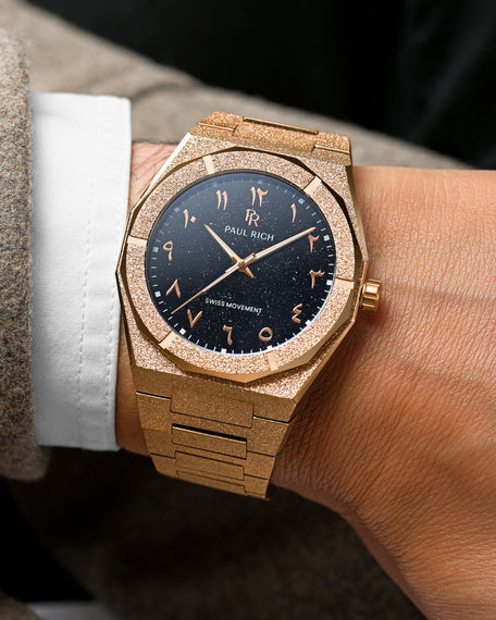 Close-up of Paul Rich rose gold frosted watch with Arabic numerals and black aventurine dial, shown on a wrist in formalwear.