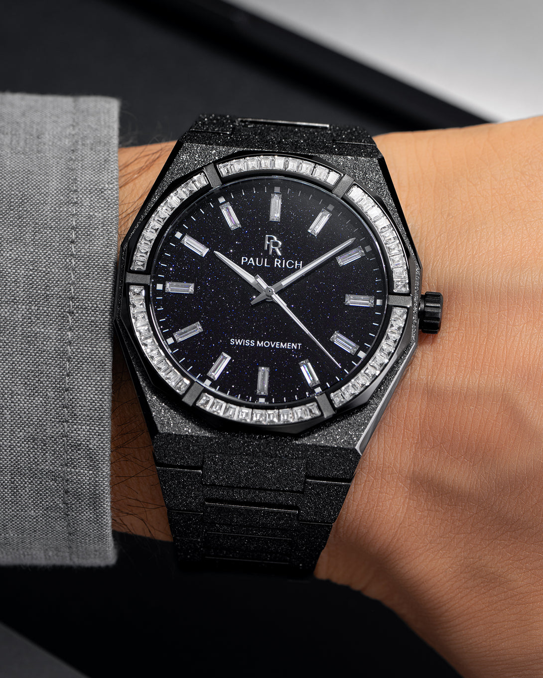 Black frosted watch with aventurine dial and moissanite bezel, worn on wrist with grey cuff.