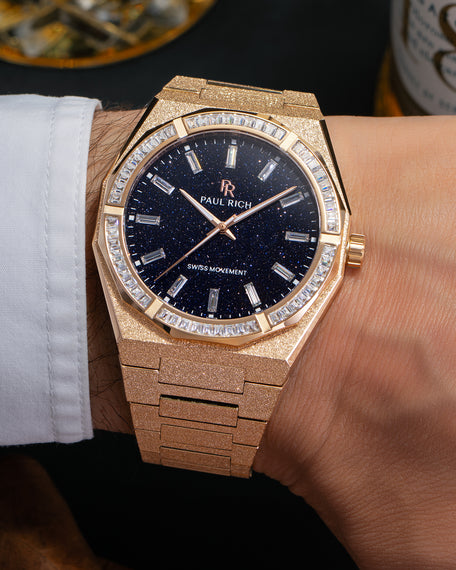 Rose gold frosted watch with aventurine dial and moissanite bezel, worn on wrist beside whiskey and cigar.