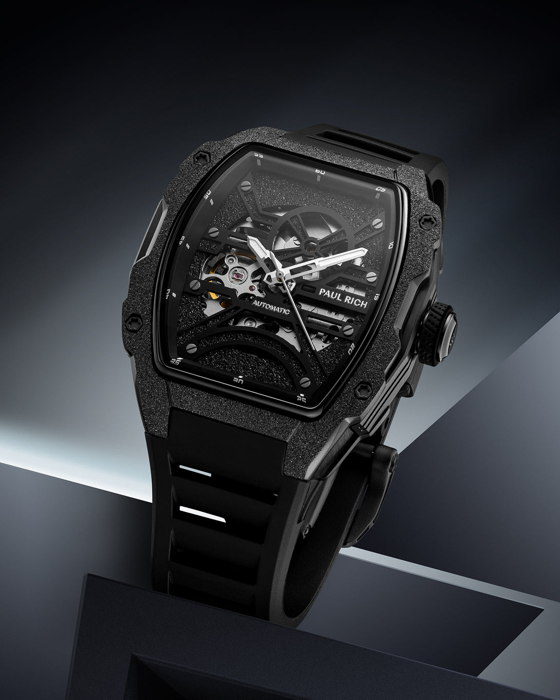 Black frosted tonneau case watch with open skeleton dial and black strap on a dark geometric background.