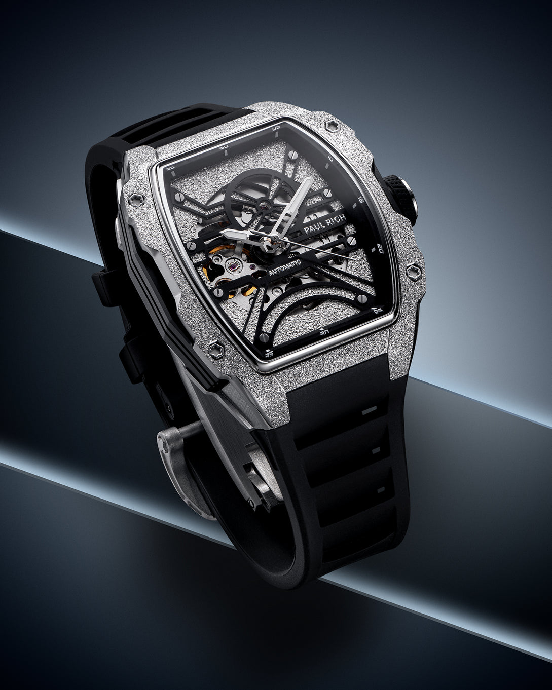 Silver frosted tonneau case watch with open skeleton dial and black strap on a dark blue geometric background.