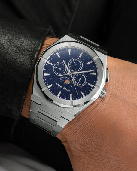 Brushed silver moonphase watch on wrist with deep blue aventurine dial, calendar subdials, and steel bracelet.