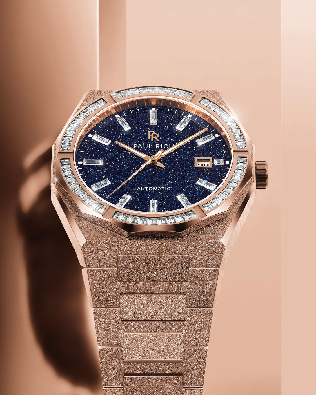Rose gold Paul Rich watch with frosted bracelet, blue aventurine dial, and gem-set bezel, displayed under warm studio lighting.