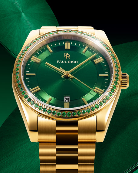 Gold watch with green sunray dial and green gemstone-set bezel on a gold bracelet, displayed against a textured green background.