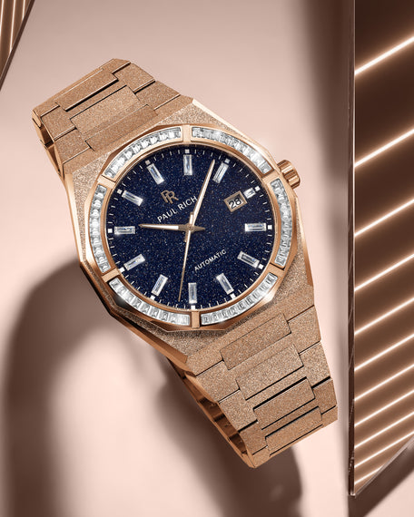 Rose gold Paul Rich watch with frosted texture, blue aventurine dial, and gem-set bezel, resting on a peach-toned reflective surface.