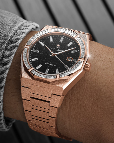 Rose gold frosted watch on a wrist with a black aventurine dial, baguette-cut stones around the bezel, and a textured rose gold bracelet.