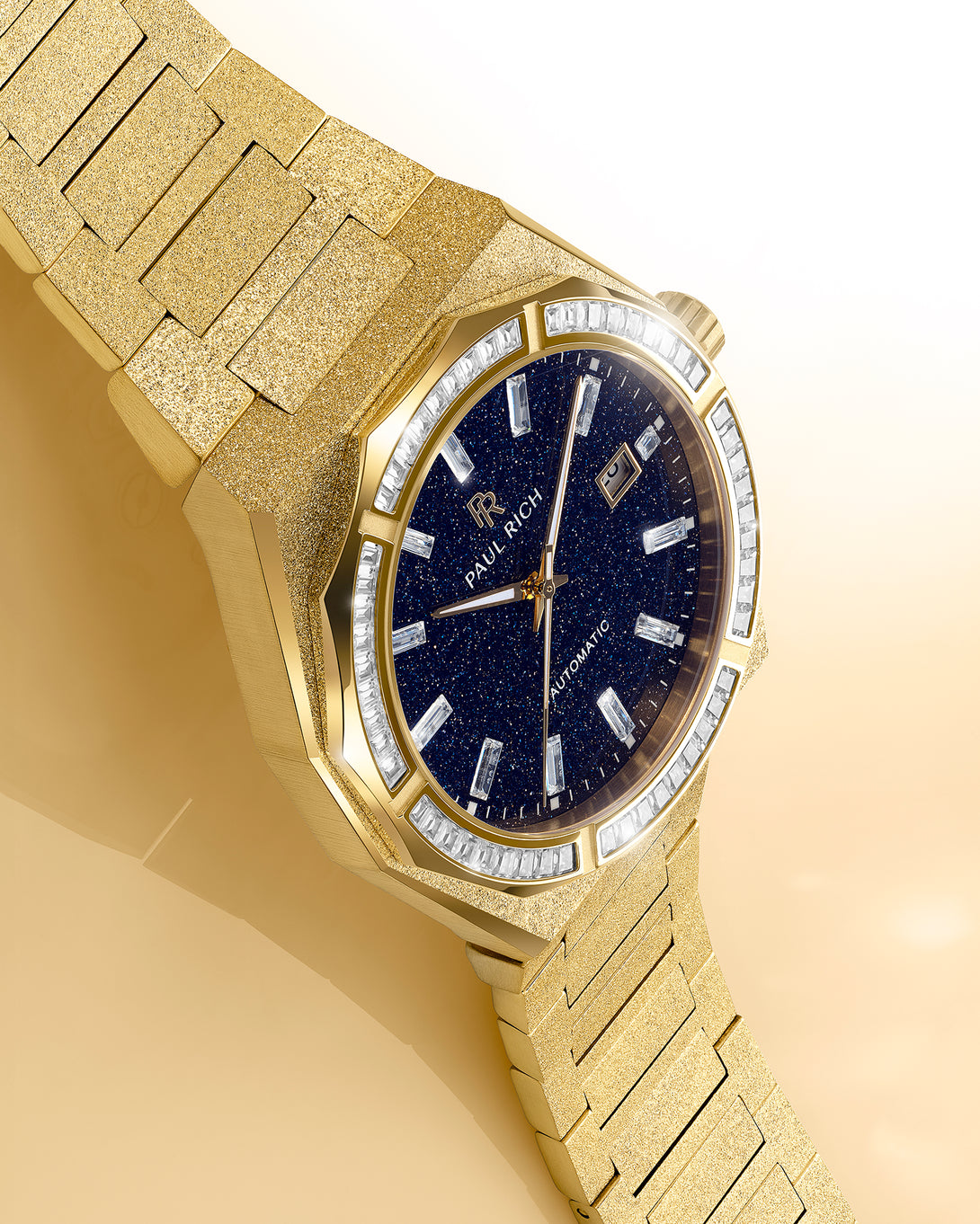 Gold frosted watch with blue aventurine dial and moissanite bezel displayed on a warm beige reflective surface under soft studio light.