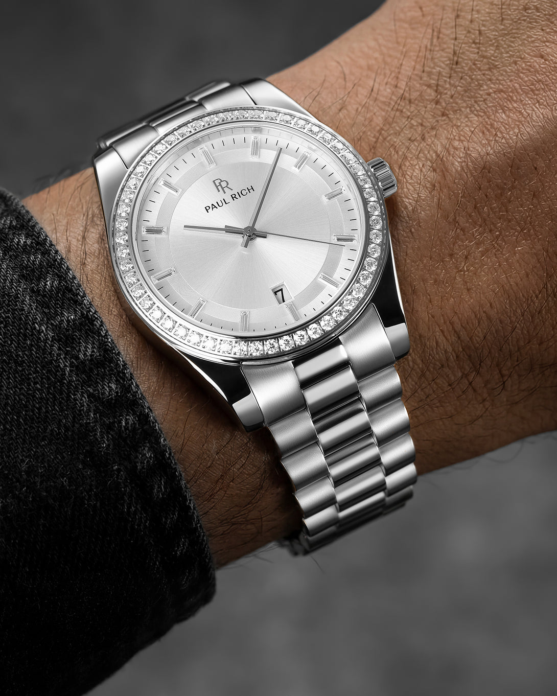 Silver watch with diamond accents on a wrist against a dark background