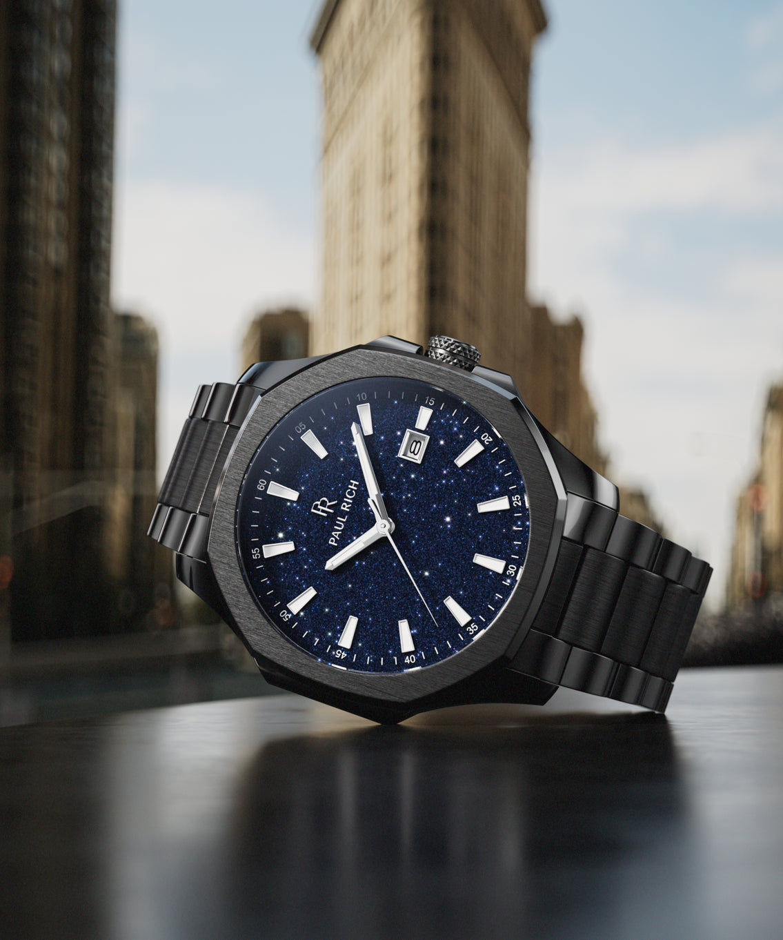 Paul Rich watch with brushed black case and blue aventurine dial displayed on a table in front of the Flatiron Building in New York City.