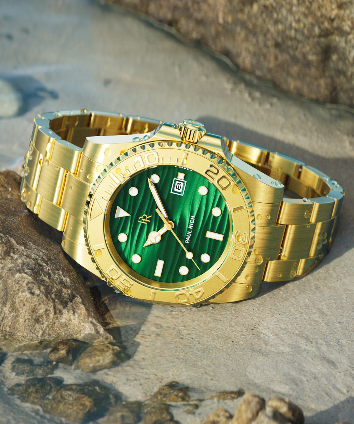 Gold dive watch with green wave-textured dial, brushed steel bracelet, rotating bezel, luminous markers, shown resting in shallow water on rocks.