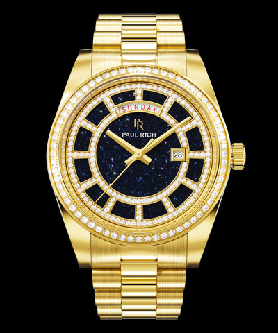 Gold watch with a blue aventurine dial, day and date windows, and a bezel and hour markers set with clear stones on a full gold bracelet.