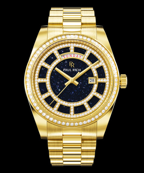 Gold watch with a blue aventurine dial, day and date windows, and a bezel and hour markers set with clear stones on a full gold bracelet.