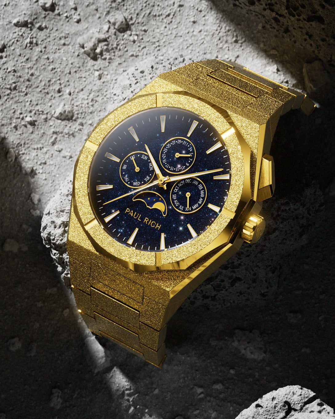 Frosted gold-tone stainless steel watch with blue aventurine dial, moonphase, and subdials, displayed on a textured grey lunar rock surface.