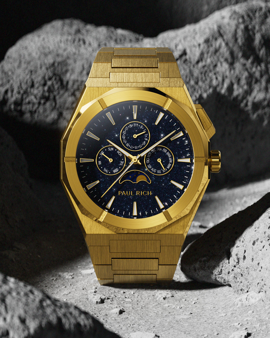 Brushed gold stainless steel watch with blue aventurine dial, moonphase, and subdials, displayed against a rugged grey lunar rock background.