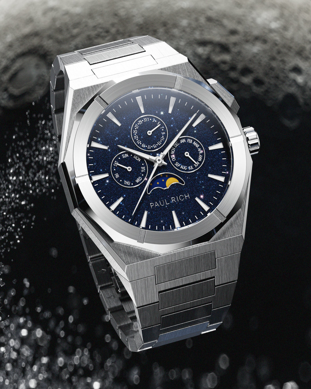 Brushed silver stainless steel watch with blue aventurine dial, moonphase, and subdials, displayed against a textured black and grey lunar surface backdrop.