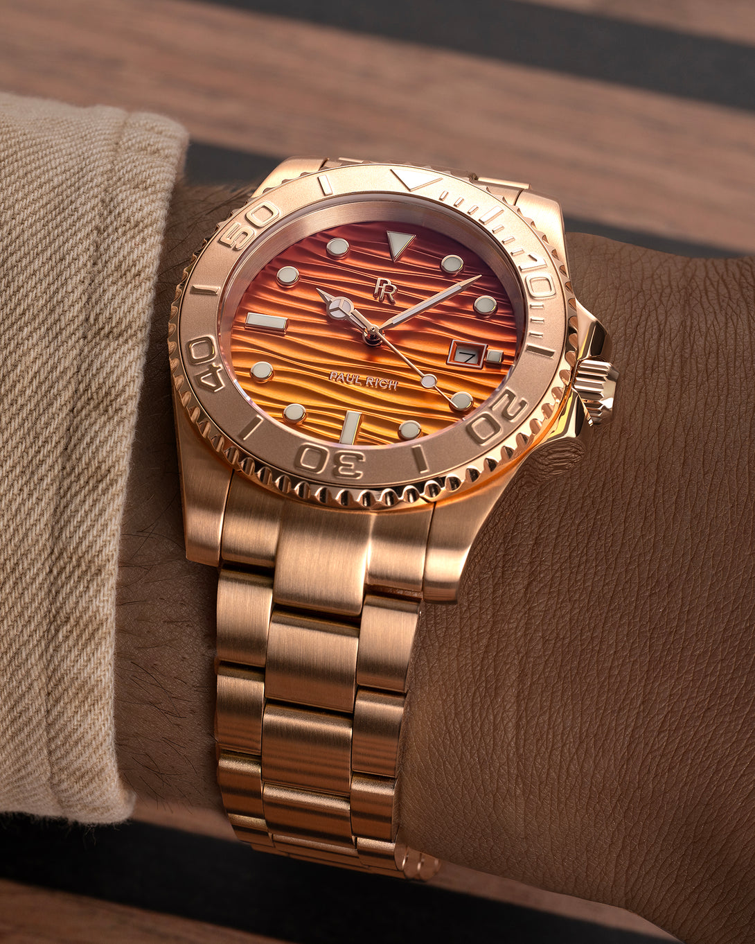 Rose-gold stainless steel watch with an orange wave-textured dial shown on a wrist, highlighting the bracelet, bezel, and dial details.