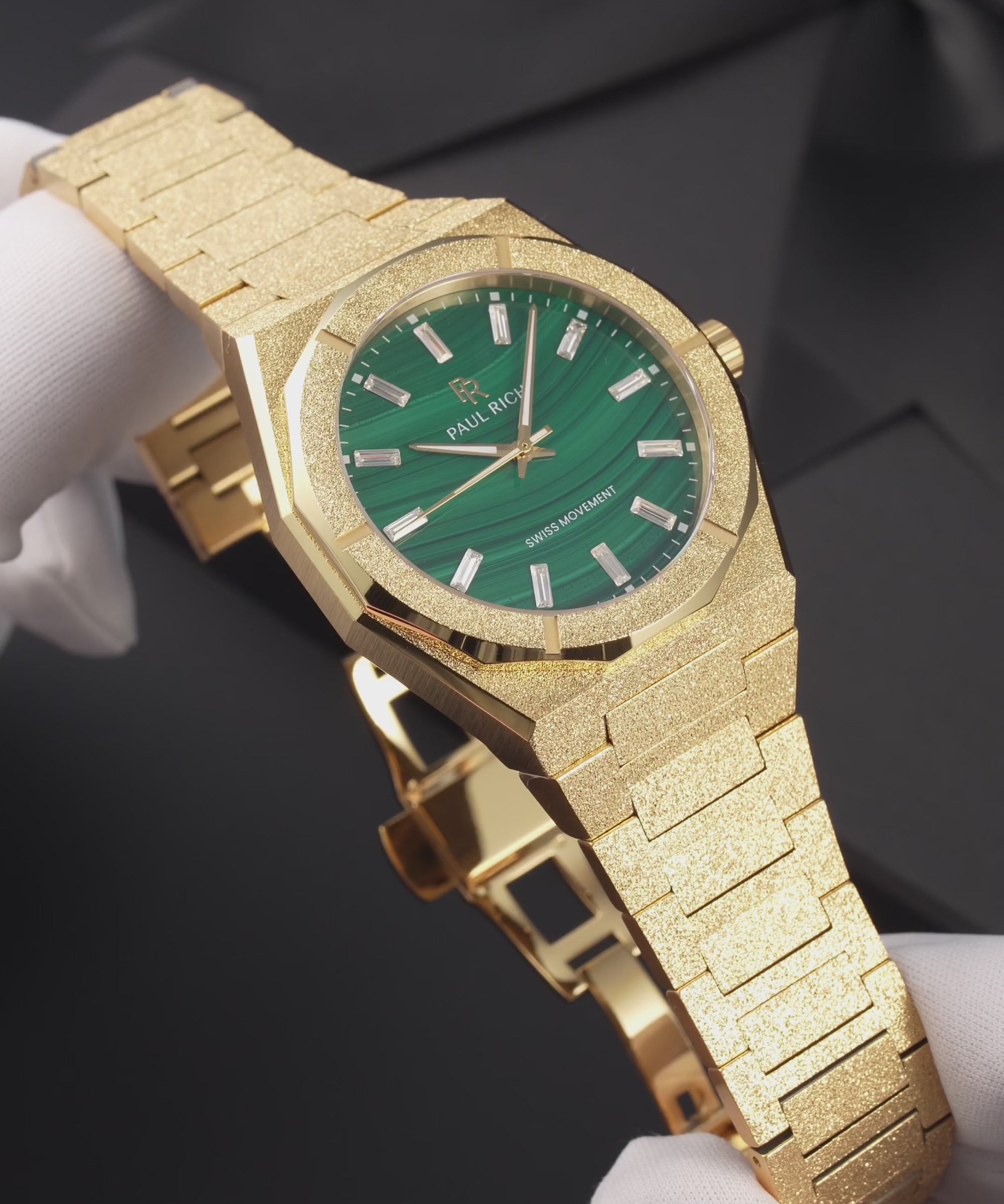 Gold-tone frosted Malachite Aurora watch with a green malachite dial, held in white gloves, worn on a wrist, lying on a black gift box and shown in close-up