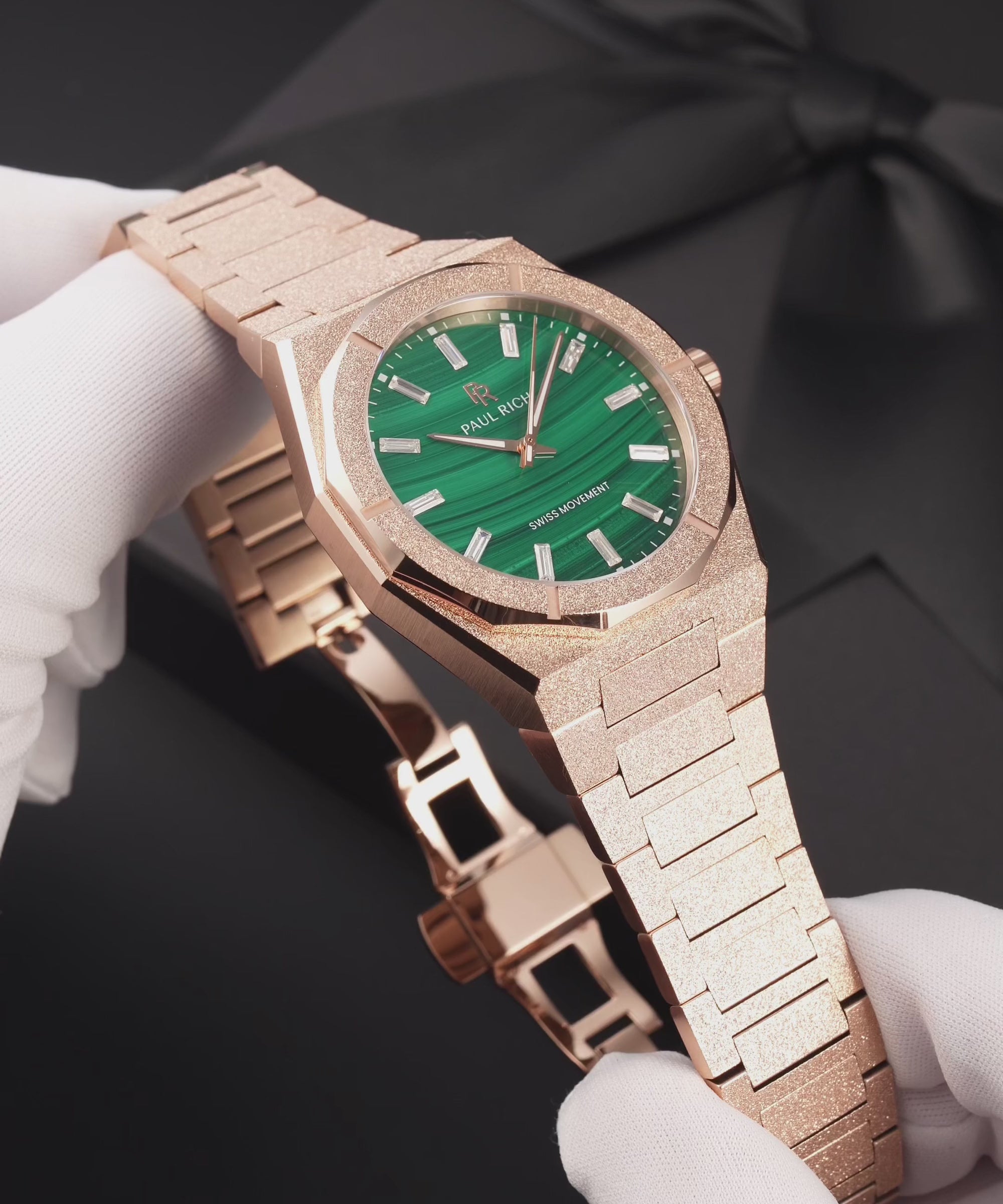 Rose-gold-tone frosted Malachite Aurora watch with a green malachite dial, held in white gloves, worn on a wrist, lying on a black gift box and shown in close-up