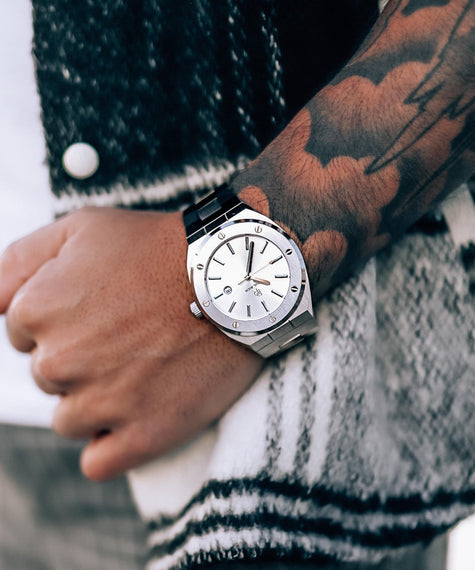 Paul Rich Apollo's Silver stainless steel watch with silver sunray dial and brushed bezel, worn on a tattooed wrist paired with a black and white textured jacket in an urban lifestyle setting.